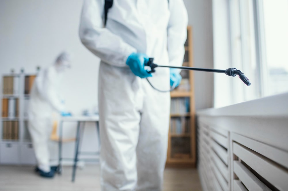 Technicien en combinaison de protection appliquant un traitement de lutte antiparasitaire résidentielle dans une chambre