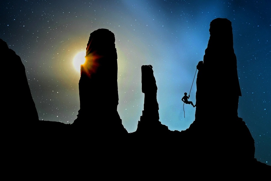 Un grimpeur en silhouette sur une paroi rocheuse sous un ciel étoilé, symbolisant les défis pour apprendre comment sécuriser votre maison contre le piratage par IA en 2026.