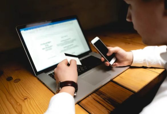 Un utilisateur effectue sa déclaration préalable en ligne sur son ordinateur portable tout en consultant son smartphone et sa carte bancaire
