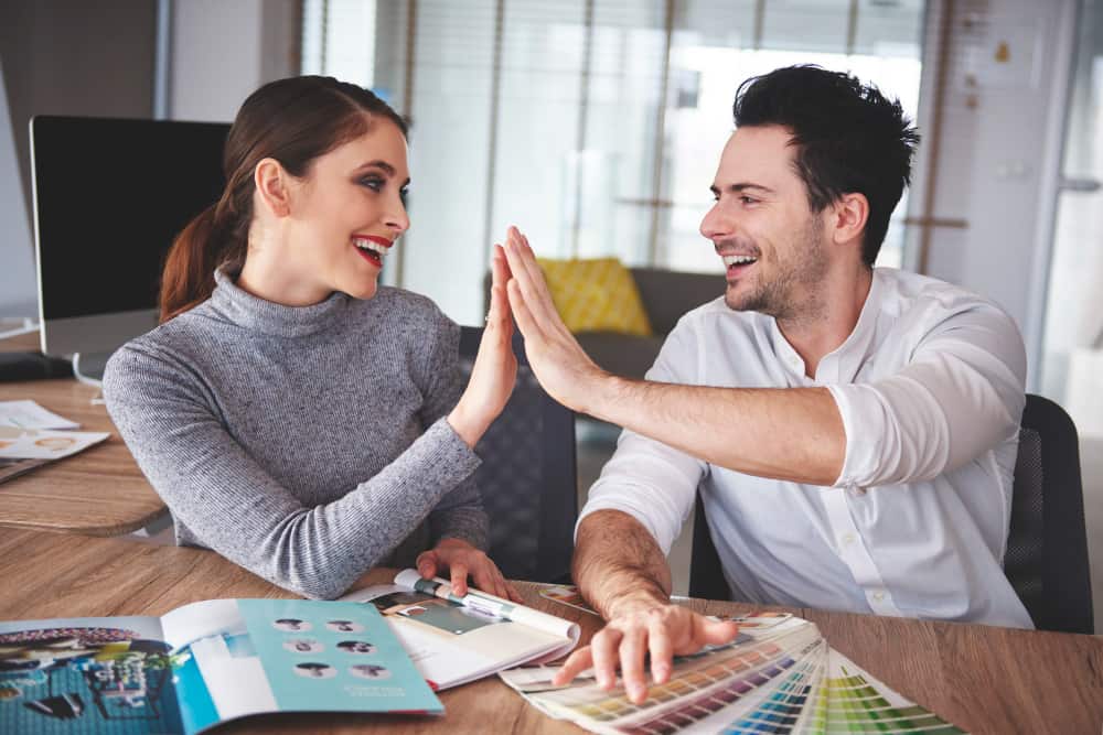 Deux collègues ou designers souriants célébrant une réussite par un high-five dans un bureau de création, illustrant l'importance de choisir le bon partenaire pour votre projet de vie professionnelle ou personnelle.
