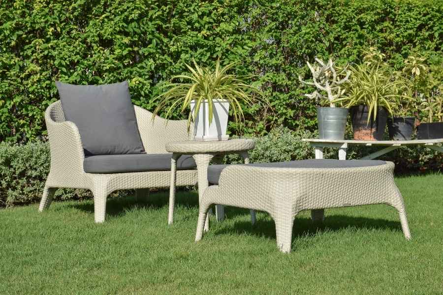 Un ensemble de mobilier en résine tressée claire avec coussins gris pour créer un salon de jardin confortable sur une pelouse.