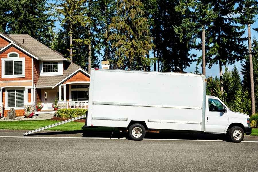 Un grand camion blanc de location de déménagement est garé avec sa rampe abaissée devant une maison individuelle.