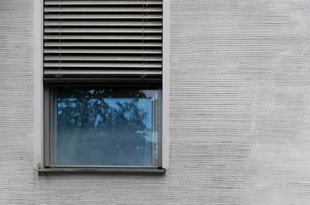 Une fenêtre moderne avec des stores extérieurs sur une façade texturée, illustrant les aspects liés à la menuiserie pvc avantage et inconvenient.